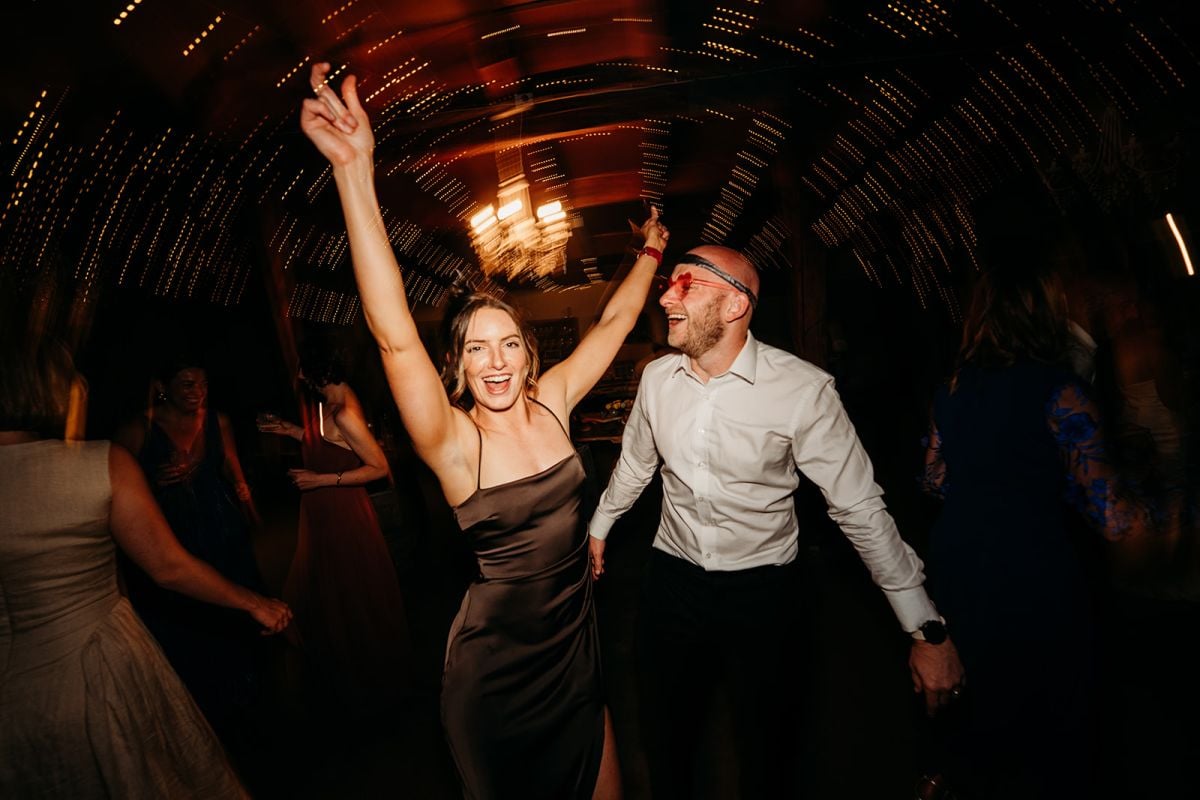 Wedding guests dancing with their hands in the air beneath fairy lights at Eileen and Patrick’s Seclusions reception.