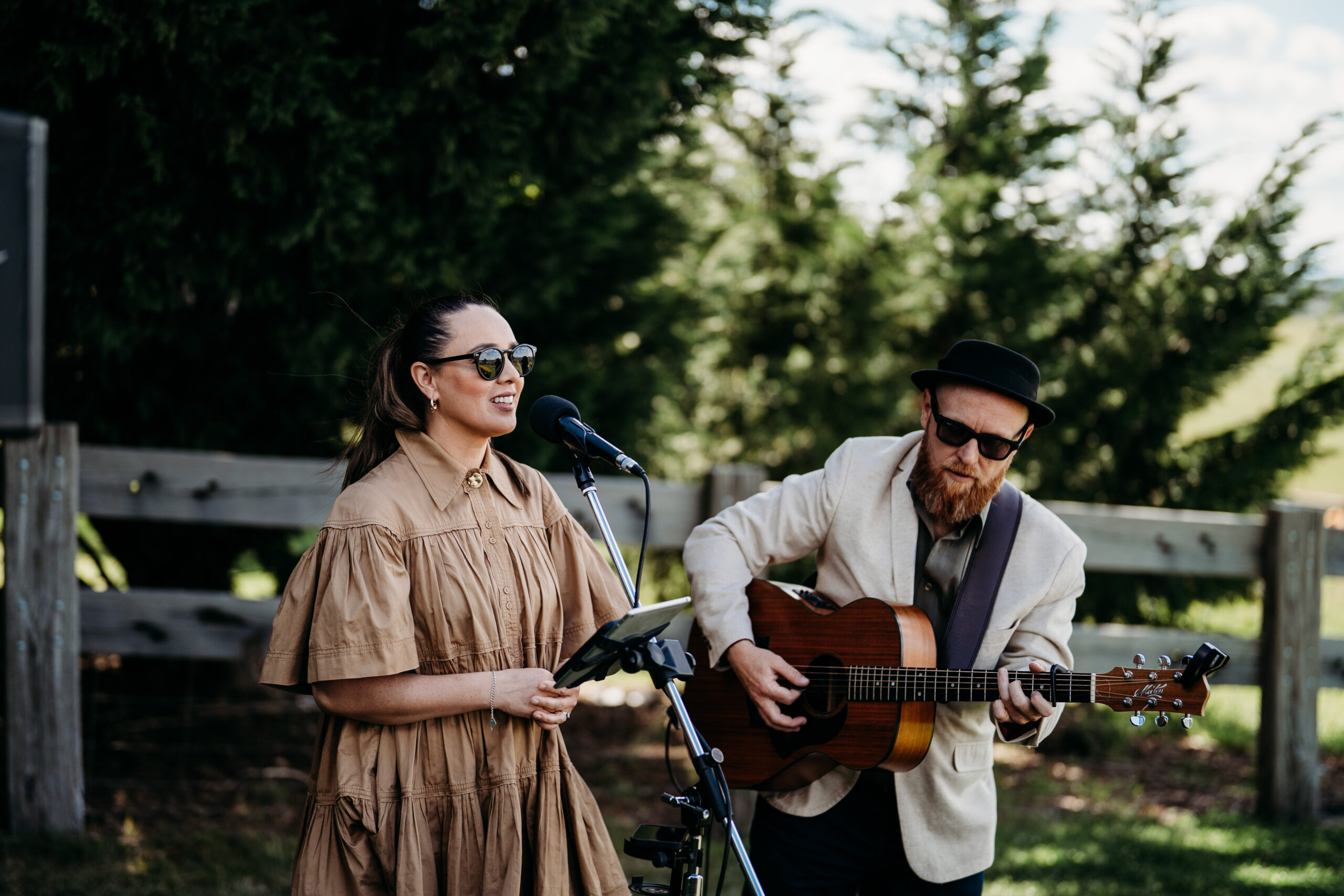 Tim and Josie performing live music in front of large green trees