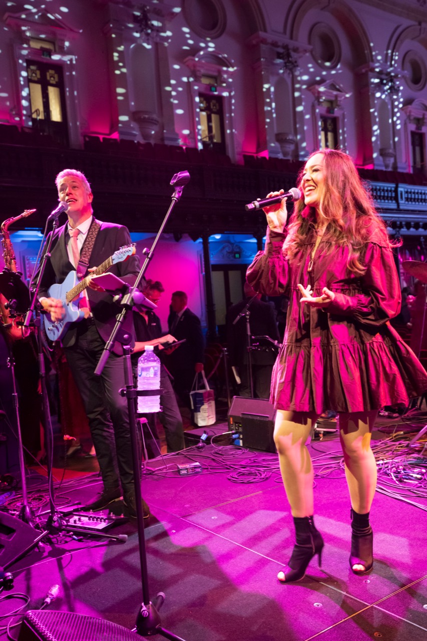 Duke Music vocalist performing with a live band under pink stage lights