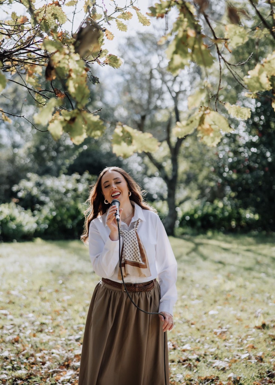 Josie singing outdoors beneath autumn leaves